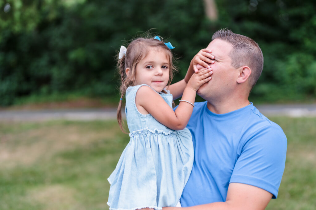 The little girl is playing with dad's face during a lifestyle outdoor family photography session by Ivy Lulu Photography in Metrowest Massachusetts