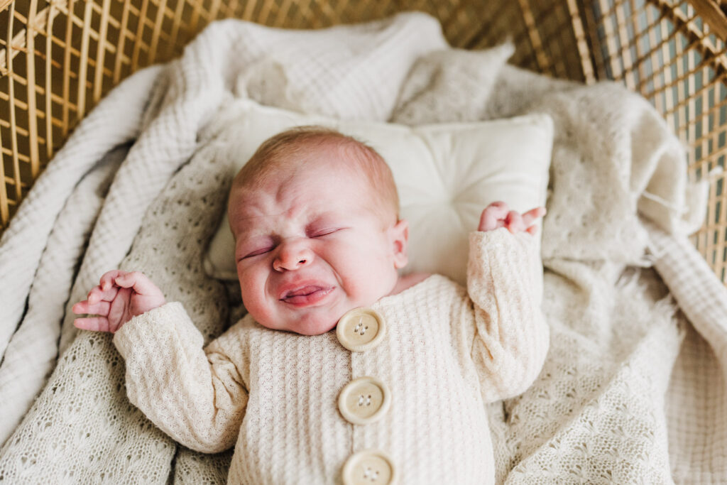 The baby is crying and feeling uncomfortable in his crib during a newborn photography session
