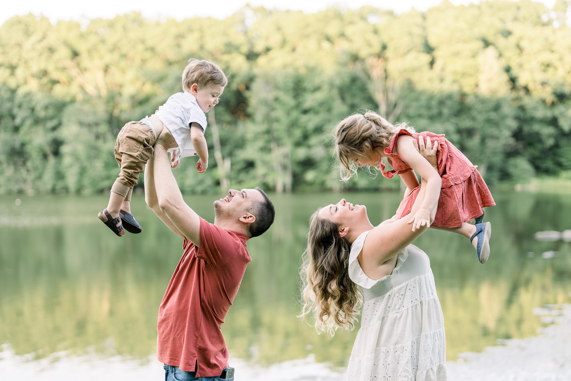 Parents lift their kids up in the air by the lake during the lifestyle family photography session at Shrewsbury, Massachusetts
