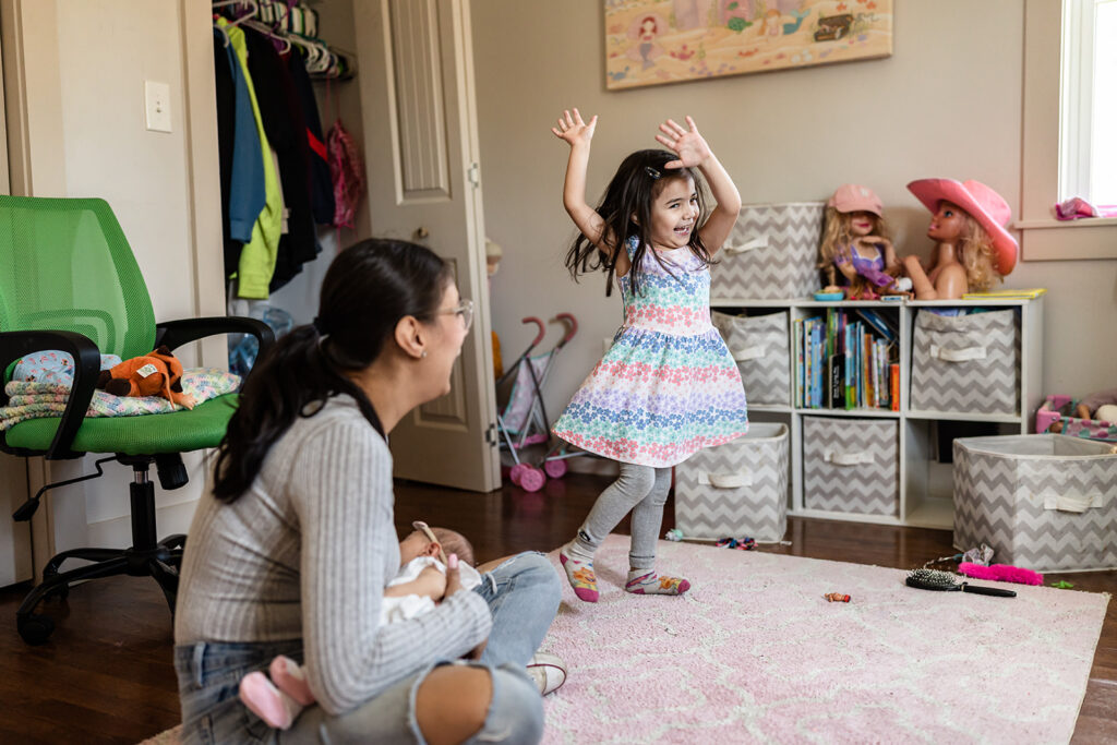 A girl is dancing while mom is breastfeeding a newborn during a documentary family photography session. 